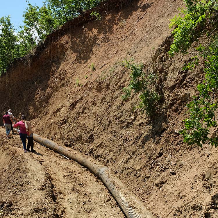A water pipe lying beneath a very steep dirt hill.