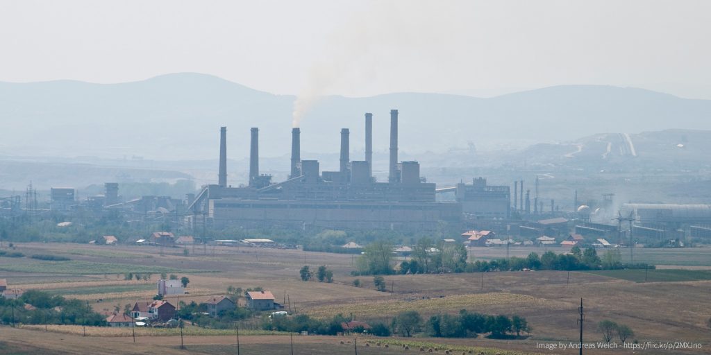 A coal power plant with 3 smoke stacks surrounded by settlements, all seen from a distance.
