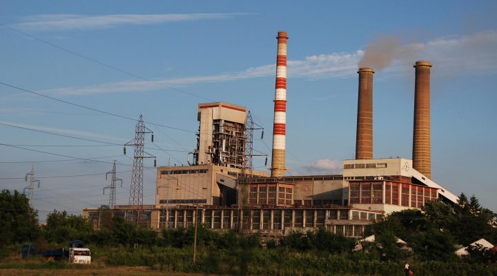 The Kolubara A coal power plant in Serbia. Three smoke stacks and a power house are seen in front of a blue sky.