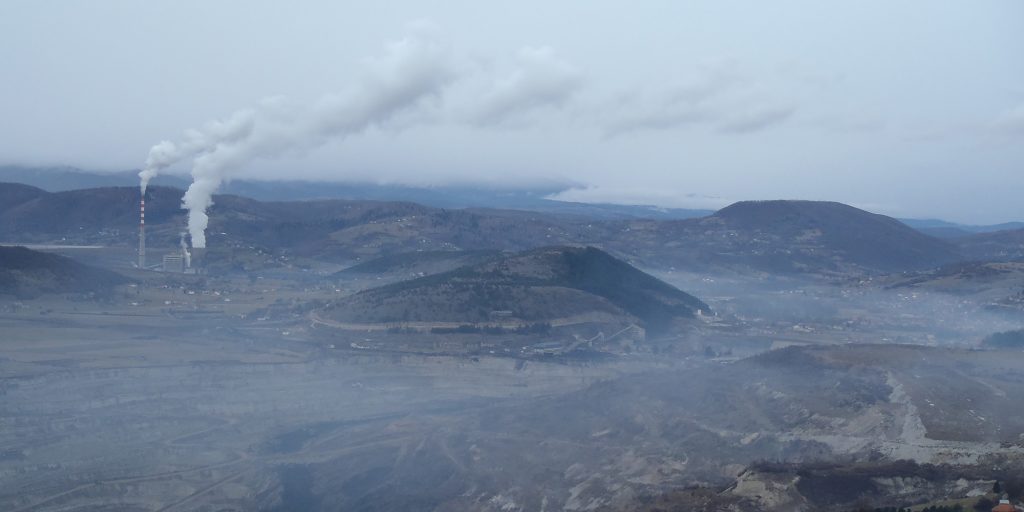 Panorama view of a valley that is dominated by a coal power plant. The smoke from the power plant's stacks fills the entire valley.