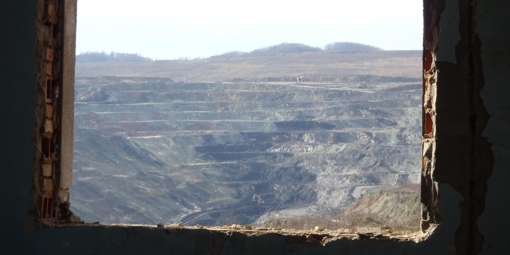 An open pit mine seen through the window of a demolished building.