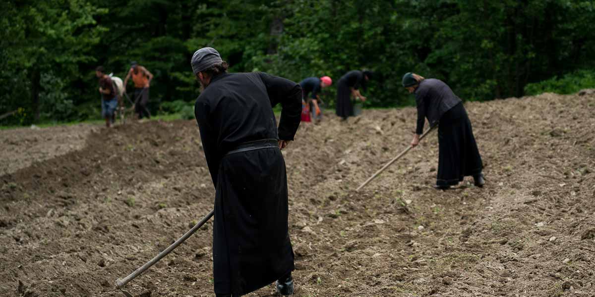 Farmers in traditional Georgian attire are doing manual work on a field.