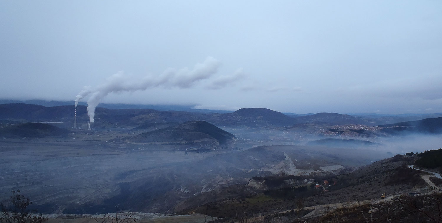 A hilly panorama showing a town submerged in smog and a coal power plant in the middle.