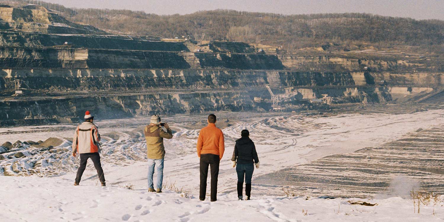 A small group of people, seen from behind, looking down into a coal mining pit.