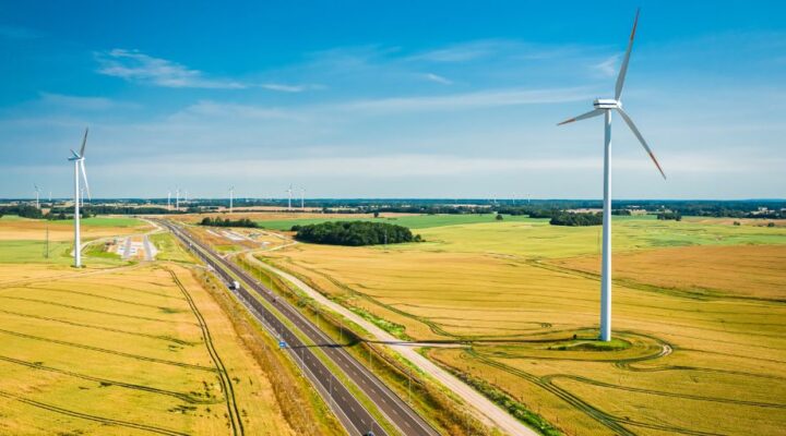 Wind turbines in yellow and green fields next to a highway